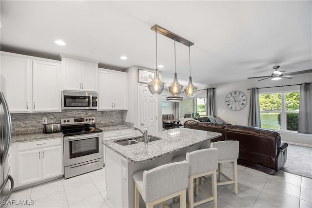 kitchen featuring light tile patterned floors, a sink, appliances with stainless steel finishes, open floor plan, and backsplash