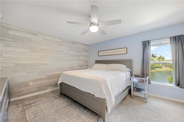 bedroom with wooden walls, baseboards, ceiling fan, an accent wall, and carpet flooring