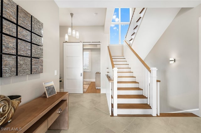 stairway with a barn door, tile patterned floors, baseboards, and a towering ceiling