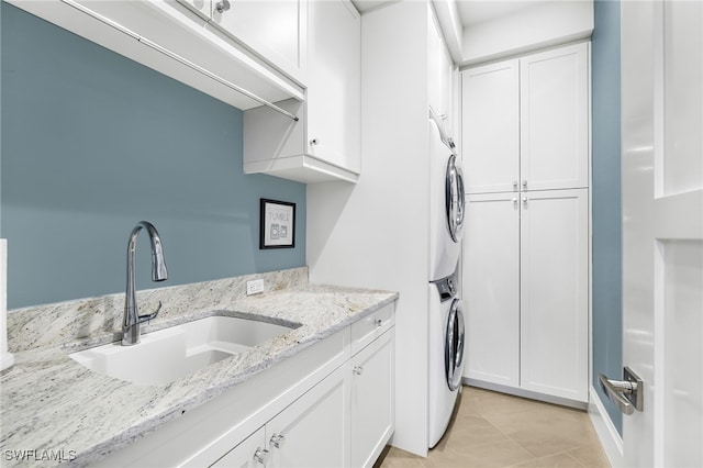 clothes washing area featuring a sink, light tile patterned flooring, cabinet space, and stacked washing maching and dryer