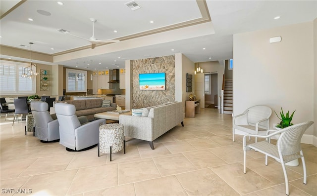 living room with visible vents, stairway, light tile patterned floors, ceiling fan with notable chandelier, and a raised ceiling