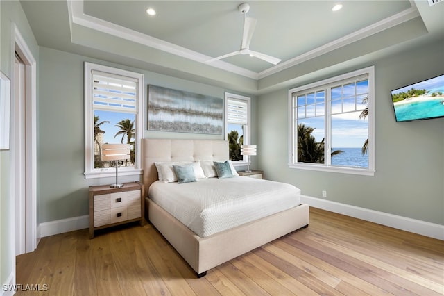 bedroom featuring light wood finished floors, a raised ceiling, and baseboards