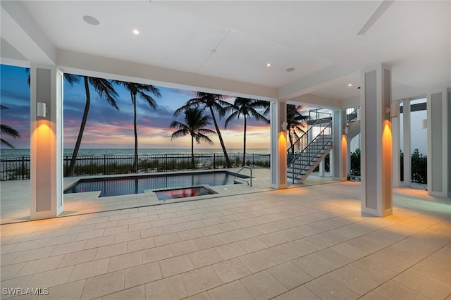 pool at dusk featuring a fenced in pool, an in ground hot tub, stairs, a water view, and a patio area