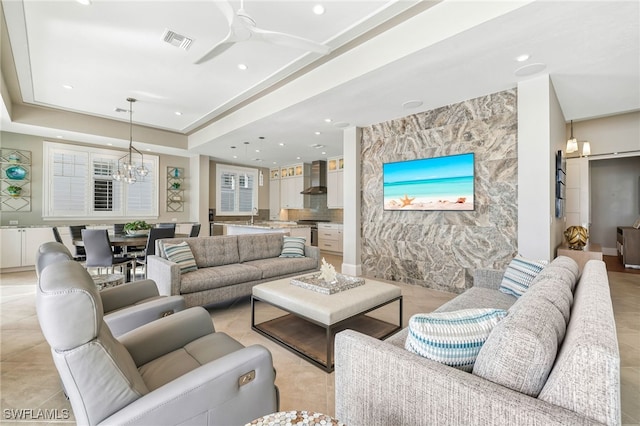 living area with visible vents, recessed lighting, an accent wall, a raised ceiling, and ceiling fan with notable chandelier