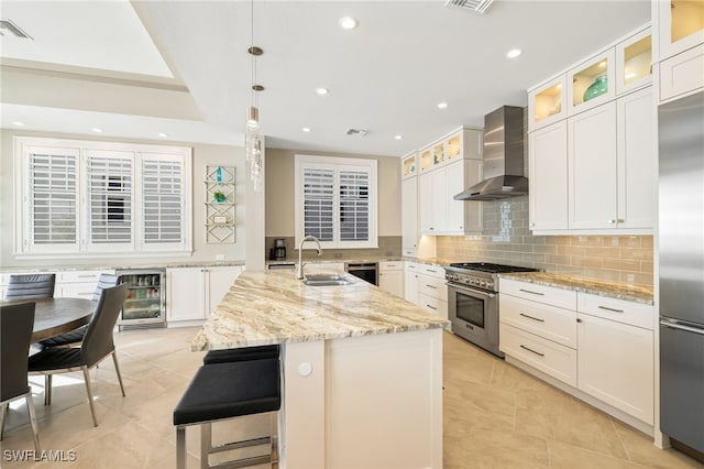 kitchen featuring a sink, premium appliances, light stone counters, and wall chimney range hood