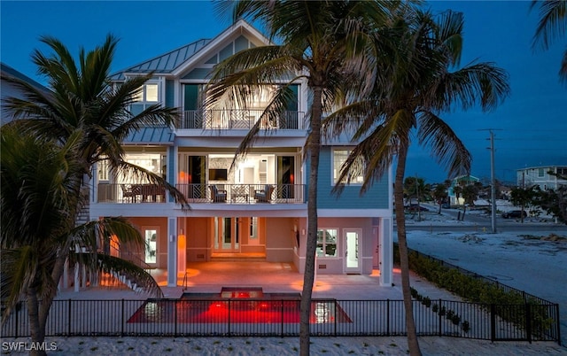 rear view of property featuring a fenced front yard, a patio, metal roof, a balcony, and a standing seam roof