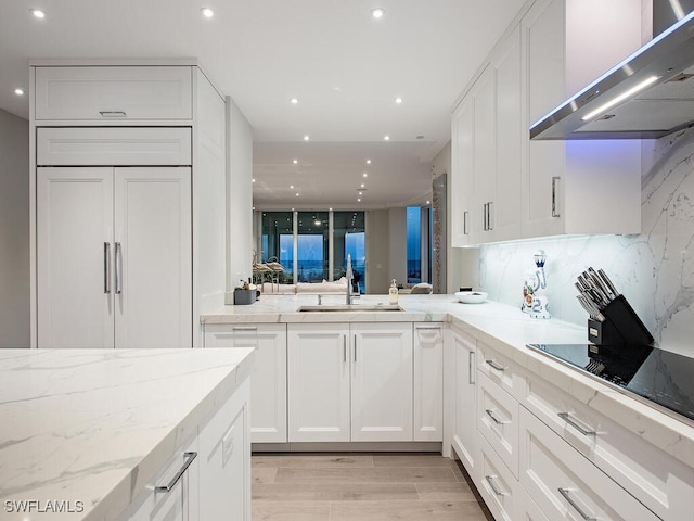 kitchen with paneled refrigerator, a sink, white cabinets, black electric stovetop, and extractor fan