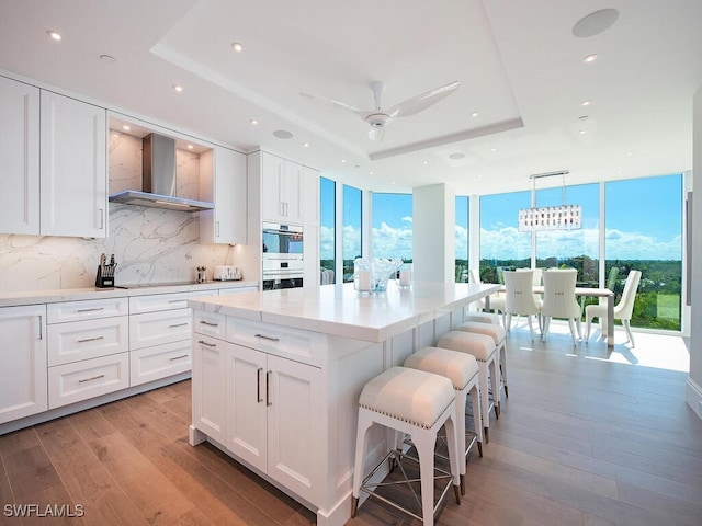 kitchen featuring light wood finished floors, a raised ceiling, wall chimney exhaust hood, and white cabinetry