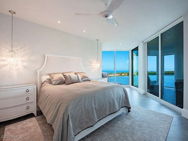 bedroom with access to exterior, a water view, floor to ceiling windows, ceiling fan with notable chandelier, and wood finished floors