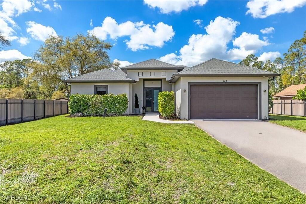 133 14th St NE, Naples, FL 34120 - prairie-style home featuring fence, driveway, stucco siding, a front lawn, and a garage