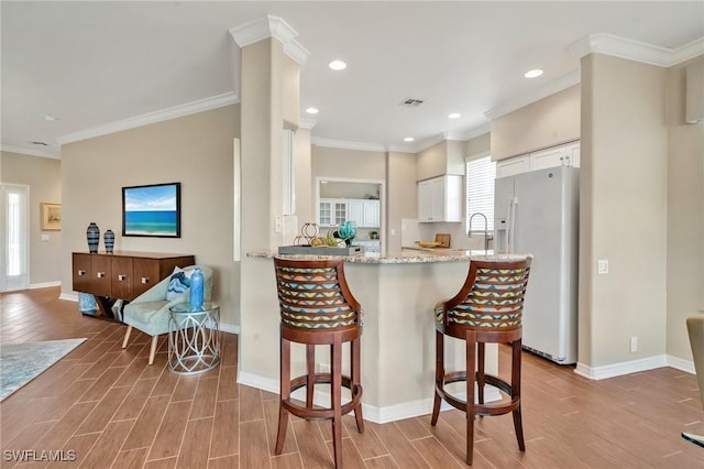 kitchen with white refrigerator with ice dispenser, wood finish floors, visible vents, white cabinets, and a kitchen bar