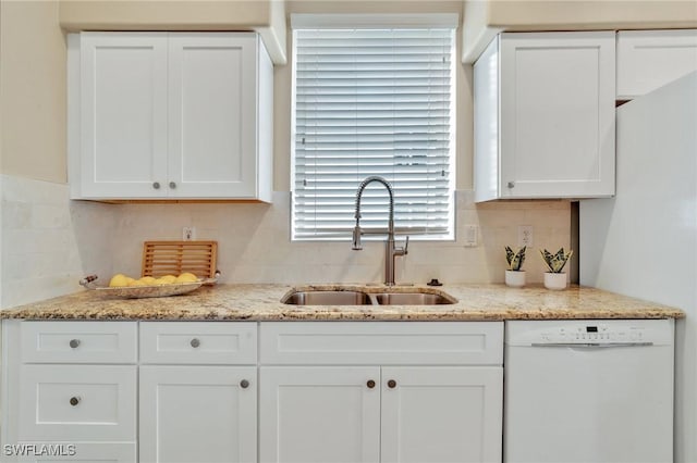 kitchen featuring light stone counters, a sink, white cabinets, backsplash, and dishwasher