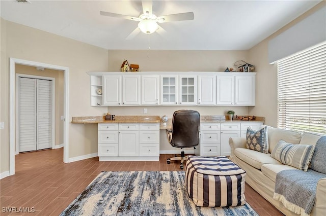 office space featuring baseboards, wood tiled floor, a ceiling fan, and built in desk