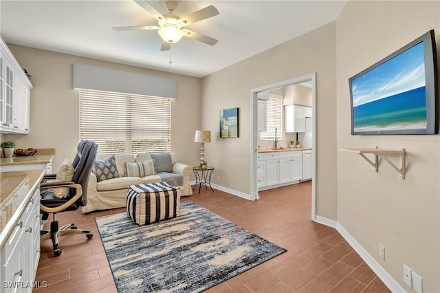 home office with a ceiling fan, baseboards, and wood finished floors