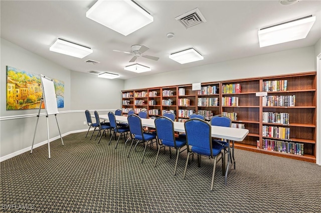 interior space featuring baseboards, wall of books, visible vents, and a ceiling fan