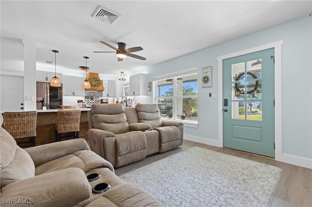 living room with ceiling fan, light wood-style floors, visible vents, and baseboards