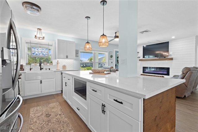 kitchen with decorative backsplash, a glass covered fireplace, open floor plan, stainless steel fridge with ice dispenser, and built in microwave