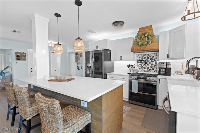 kitchen with light wood-type flooring, a kitchen bar, decorative backsplash, appliances with stainless steel finishes, and custom exhaust hood