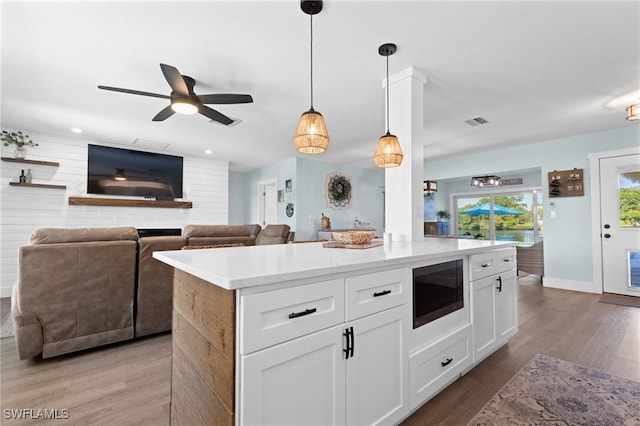 kitchen with visible vents, built in microwave, pendant lighting, wood finished floors, and white cabinets