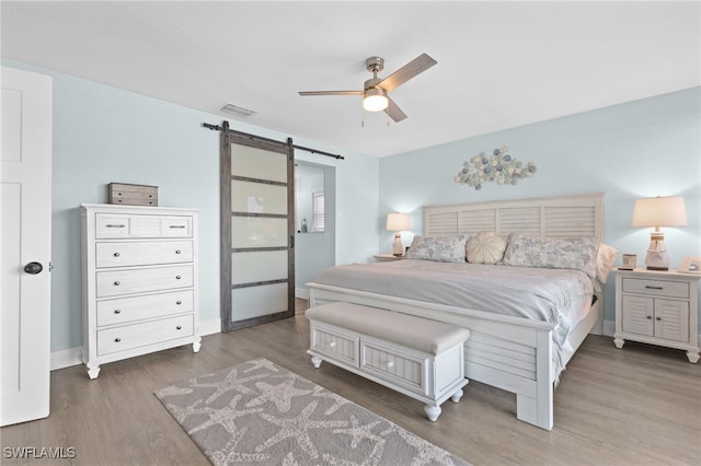 bedroom featuring a ceiling fan, wood finished floors, visible vents, baseboards, and a barn door