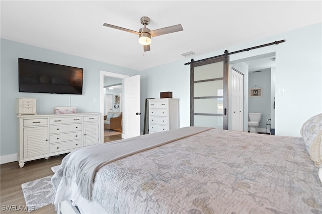 bedroom featuring visible vents, ensuite bathroom, wood finished floors, a barn door, and ceiling fan