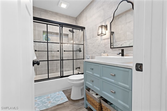 full bath with vanity, wood finished floors, tile walls, toilet, and combined bath / shower with glass door