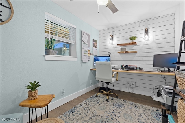 office space featuring wood finished floors, wooden walls, baseboards, ceiling fan, and built in study area