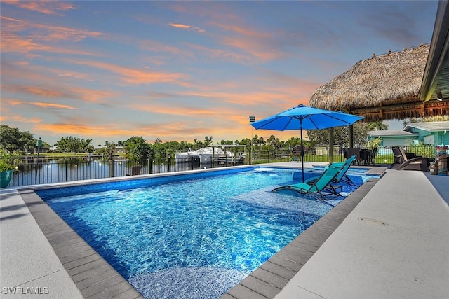 pool at dusk featuring a patio area, fence, a fenced in pool, and a water view