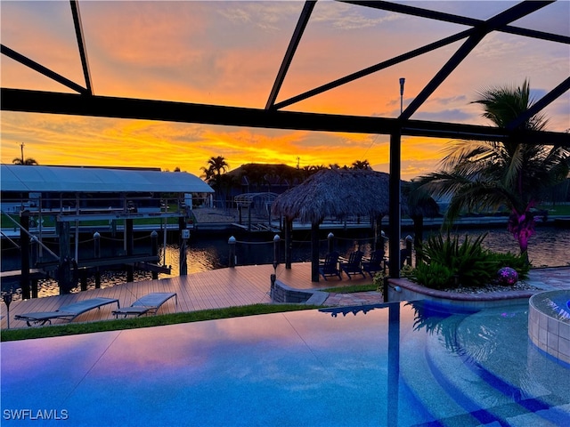 pool at dusk featuring an outdoor pool, a boat dock, boat lift, a water view, and a lanai