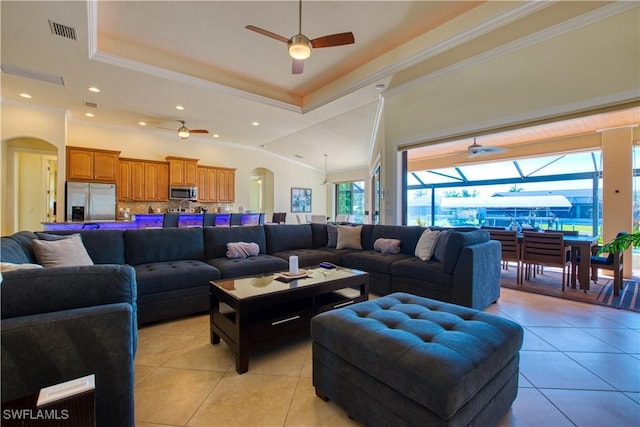 living room featuring light tile patterned floors, visible vents, arched walkways, ornamental molding, and a tray ceiling