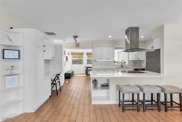 kitchen featuring island exhaust hood, a kitchen breakfast bar, white cabinets, and freestanding refrigerator