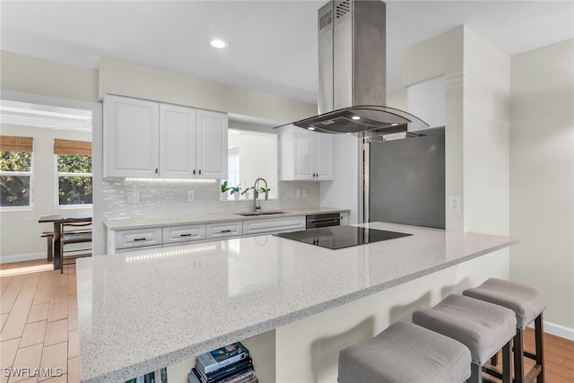 kitchen featuring black electric stovetop, freestanding refrigerator, a sink, island range hood, and a kitchen breakfast bar