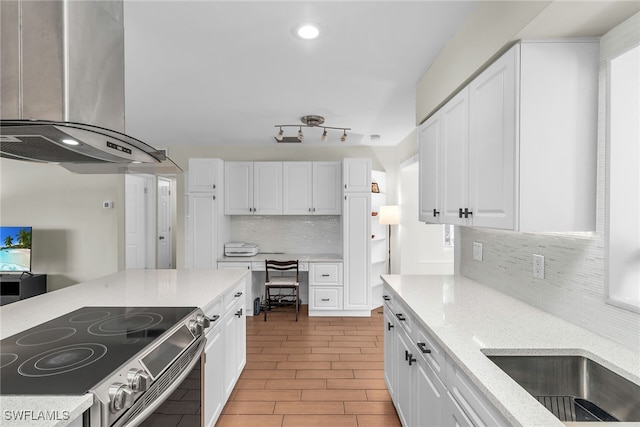 kitchen featuring electric range, white cabinets, built in study area, light stone countertops, and wall chimney exhaust hood