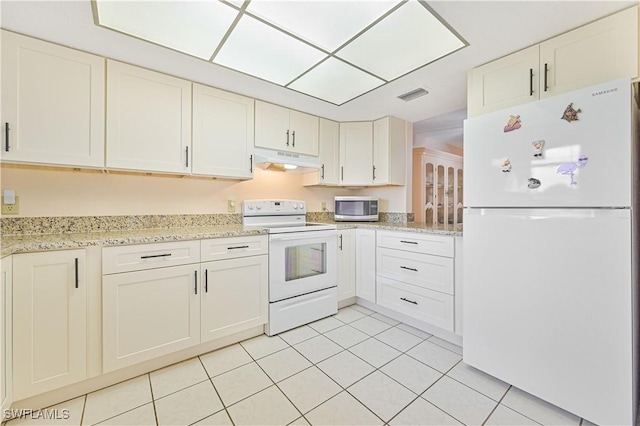 kitchen with light tile patterned flooring, under cabinet range hood, white appliances, visible vents, and light stone countertops