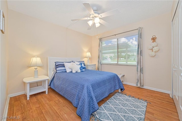 bedroom with ceiling fan, a textured ceiling, baseboards, and wood finished floors