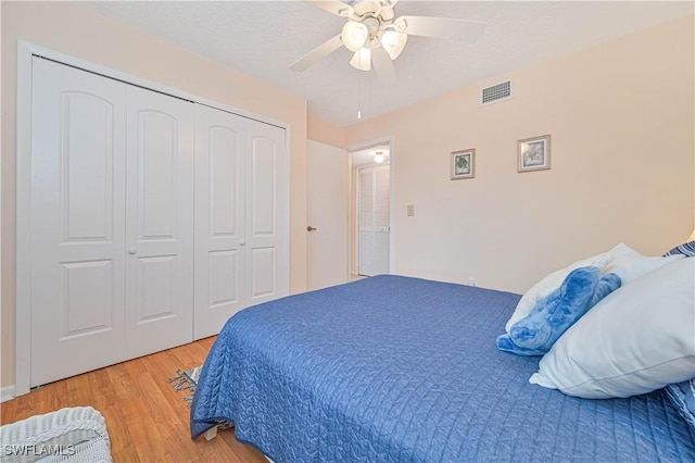 bedroom with a closet, visible vents, light wood-style floors, ceiling fan, and a textured ceiling