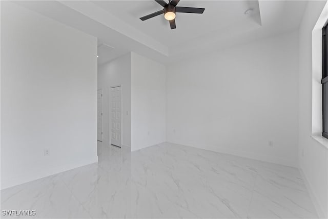 empty room with marble finish floor, baseboards, a tray ceiling, and a ceiling fan