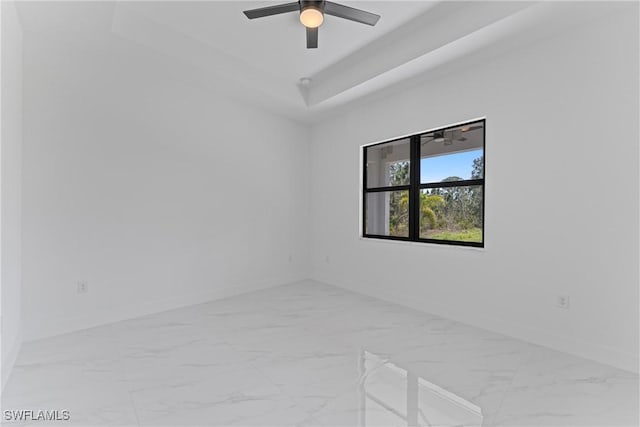 empty room featuring a ceiling fan, a tray ceiling, marble finish floor, and baseboards