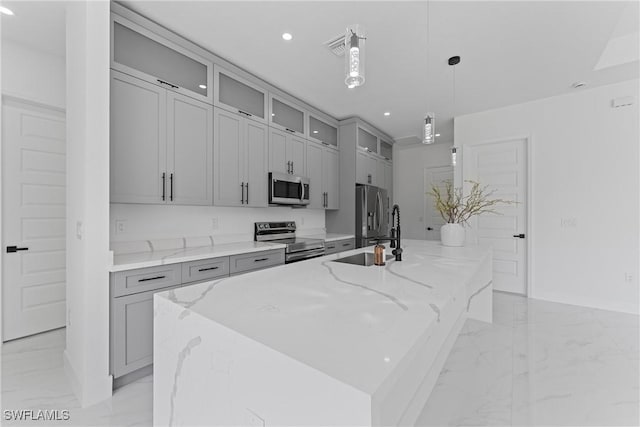 kitchen with an island with sink, marble finish floor, stainless steel appliances, gray cabinetry, and a sink