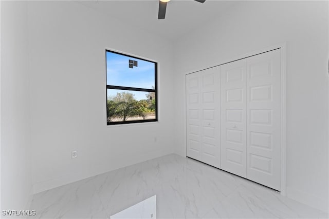 unfurnished bedroom with a ceiling fan, marble finish floor, a closet, and baseboards