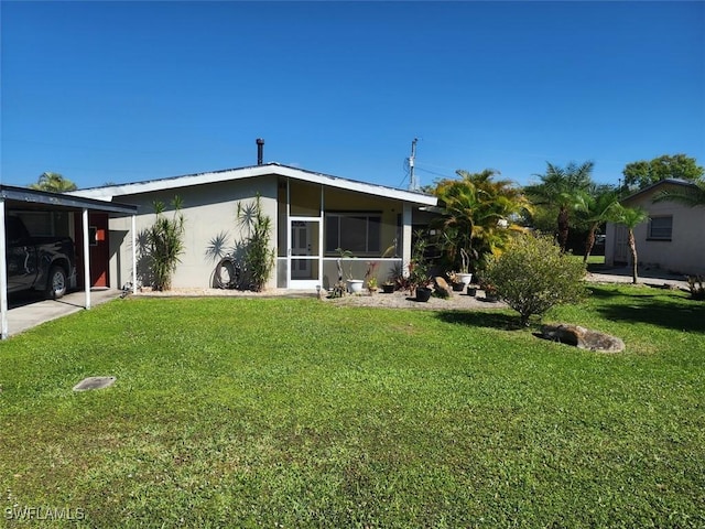 back of property featuring a carport, a lawn, a sunroom, and stucco siding