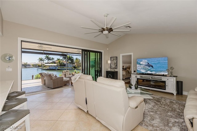 living area featuring a fireplace, light tile patterned floors, lofted ceiling, a water view, and a ceiling fan