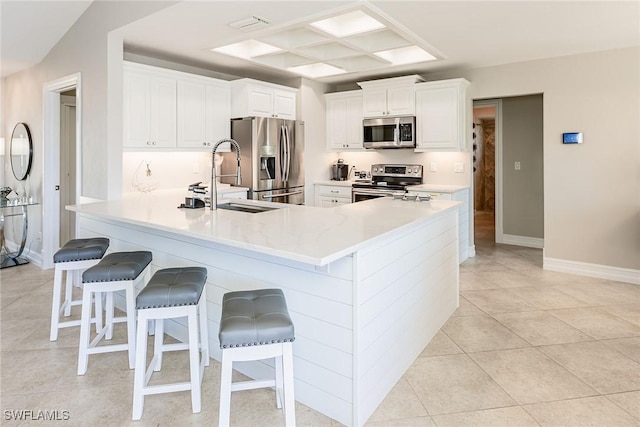 kitchen featuring baseboards, stainless steel appliances, light countertops, a kitchen bar, and white cabinetry