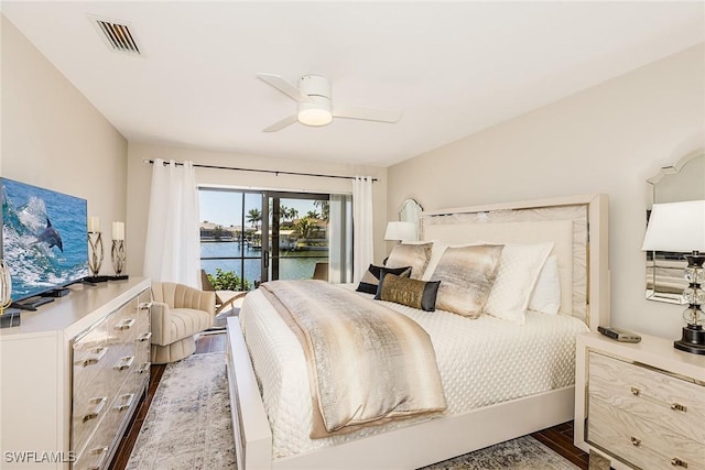 bedroom featuring a water view, a ceiling fan, visible vents, and wood finished floors