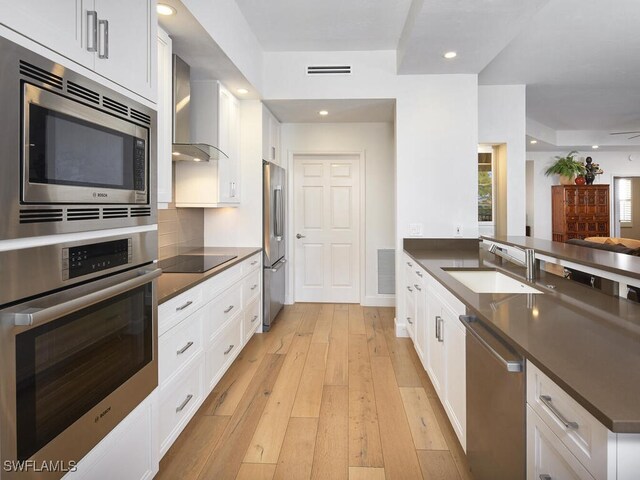 kitchen with visible vents, dark countertops, appliances with stainless steel finishes, wall chimney range hood, and a sink