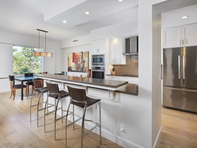 kitchen with wall chimney range hood, tasteful backsplash, stainless steel appliances, and light wood finished floors