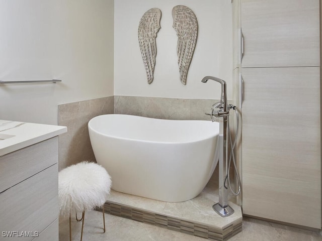 full bathroom featuring tile walls, a soaking tub, wainscoting, and vanity