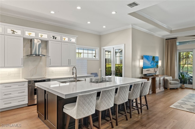 kitchen with visible vents, light wood-style flooring, an island with sink, electric stove, and wall chimney exhaust hood