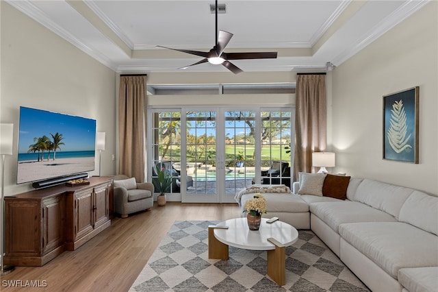 living area with a tray ceiling, visible vents, crown molding, and light wood finished floors