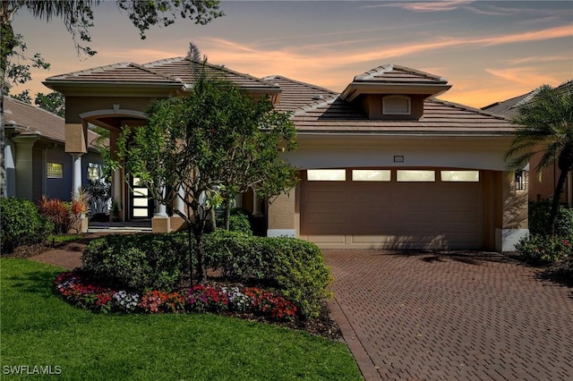 view of front of home featuring stucco siding, an attached garage, a tile roof, and decorative driveway